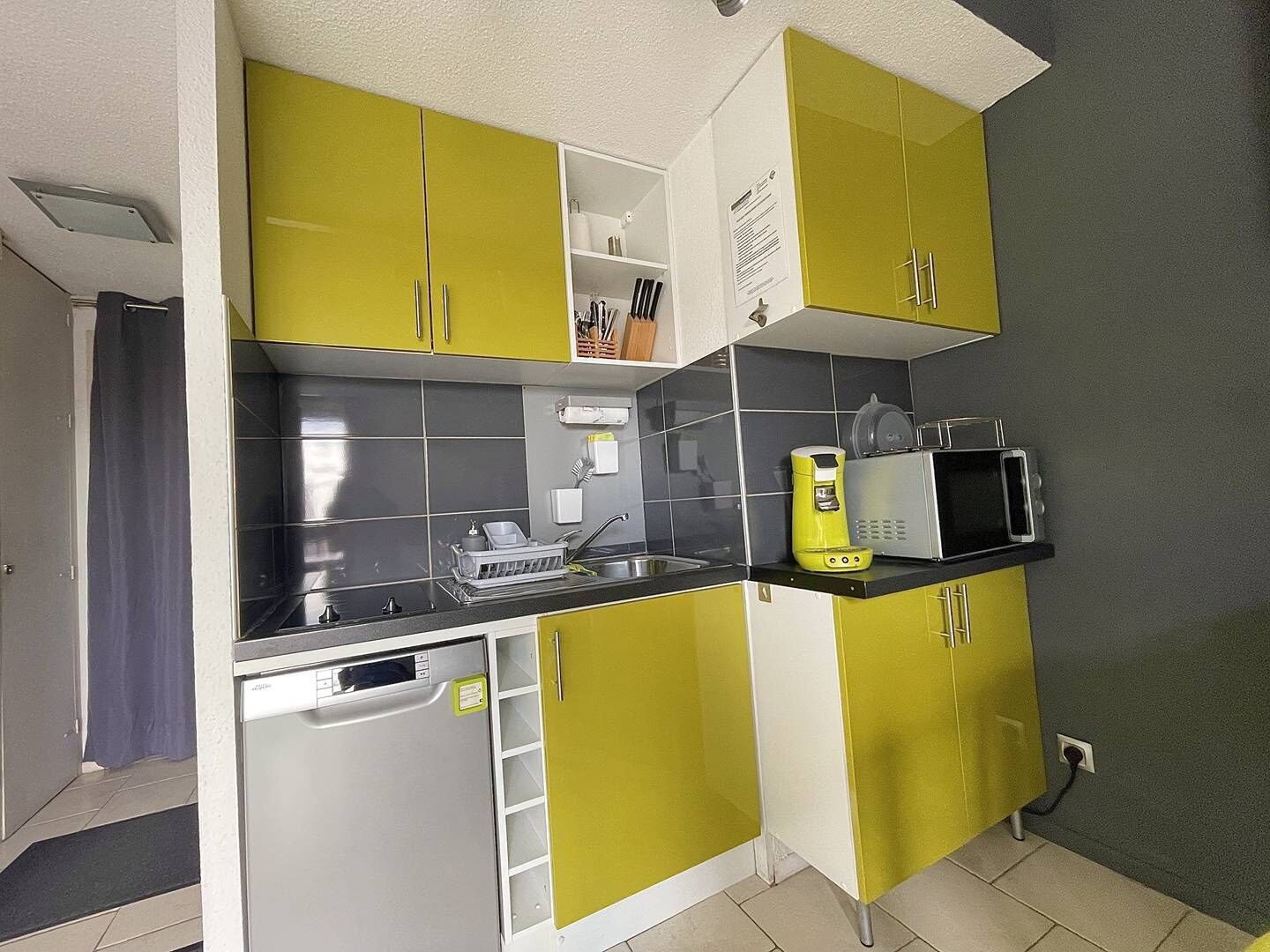 A compact kitchen with yellow cabinets, a microwave, and a dishwasher.