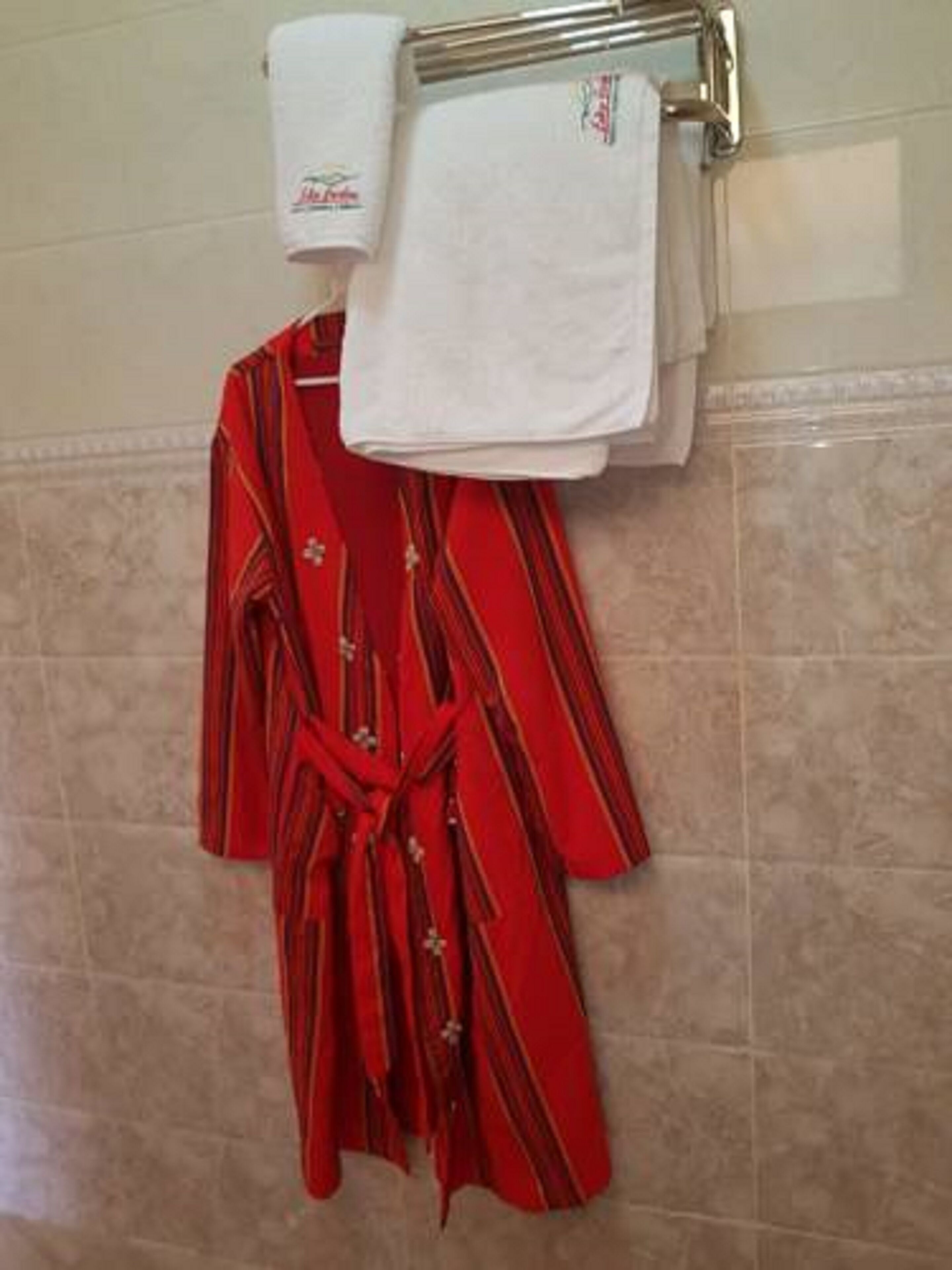 A bathroom with a towel rack holding a red robe and two white towels.