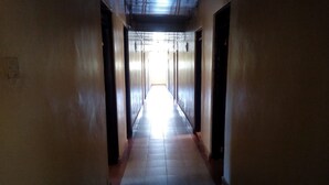 Un pasillo largo y estrecho con suelo de baldosas y puertas a ambos lados, que desemboca en un espacio luminoso al final.