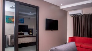 A modern hotel room with a bed, a red sofa, a TV, and a large mirror. - The Lodge by Kabachi (Lagos)