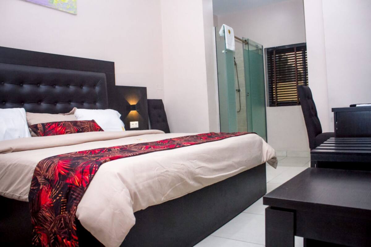 A hotel room with a large bed, a desk, and a shower area.