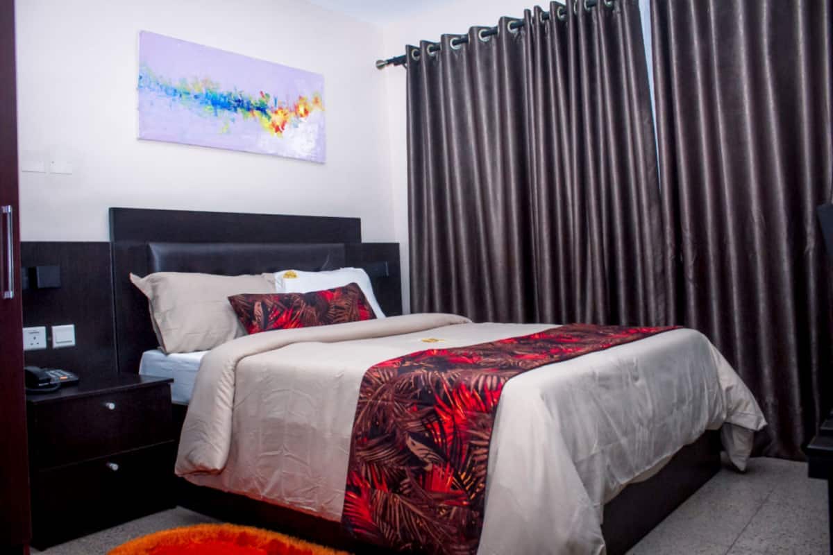 A bedroom with a bed, a nightstand, a lamp, a painting on the wall, and curtains.