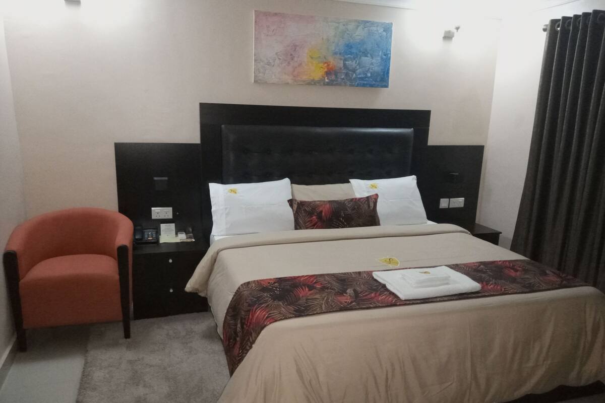 A hotel room with a bed, a nightstand, a chair, and a painting on the wall.