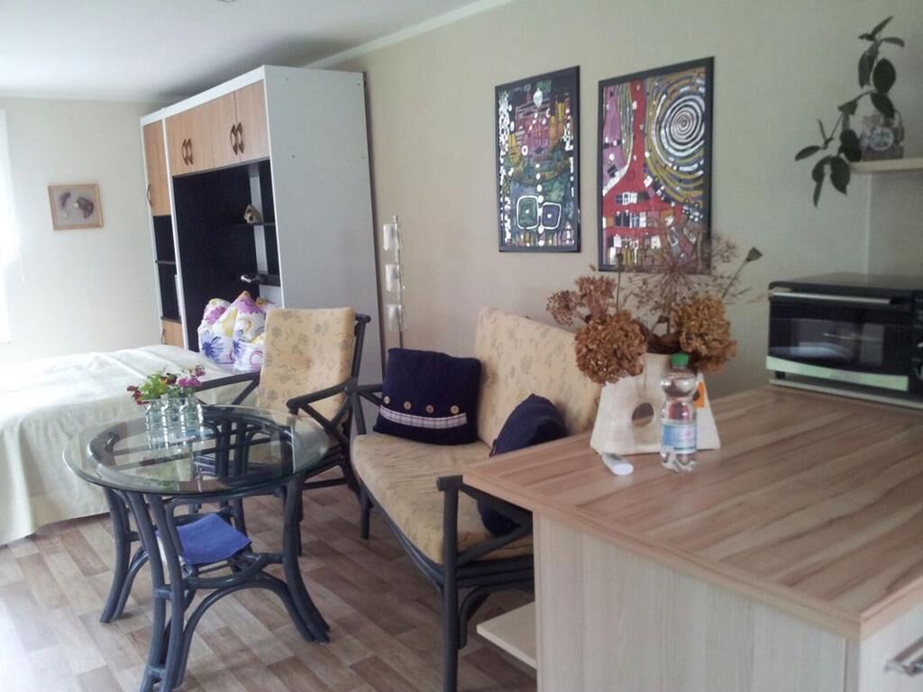 A living room with a glass table, two chairs, a sofa, a wooden coffee table, a cabinet, and two wall art pieces.