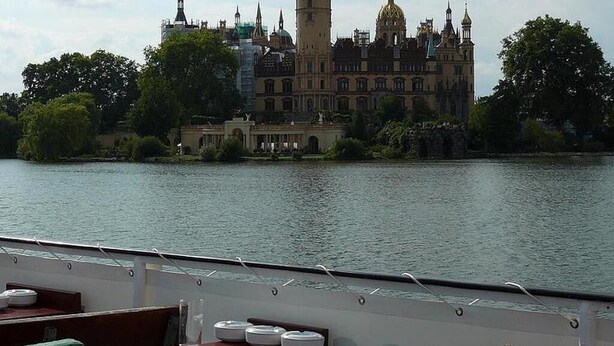 A historic building with a prominent tower and domed roof, situated by a calm body of water. - Your apartment in the countryside on Lankower See in Schwerin Mecklenburg... (Schwerin)