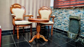 Two wooden chairs with cushioned seats and backs, a round wooden table, and a tiled floor. - Power Mike Guest House (Abuja)