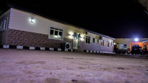 A two-story building with a flat roof, a brick lower section, and a white upper section. There are multiple windows and a door with a light fixture above it. - Power Mike Guest House (Abuja)