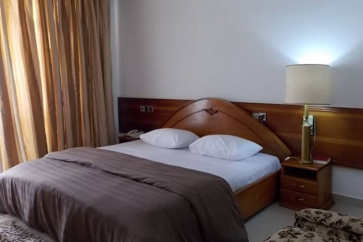 A neatly made bed with a brown headboard, a bedside lamp, and a nightstand with a lamp.