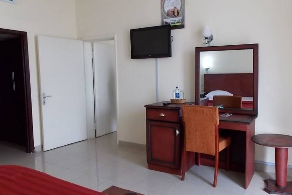 A hotel room with a bed, a desk with a chair, a television, and a mirror.