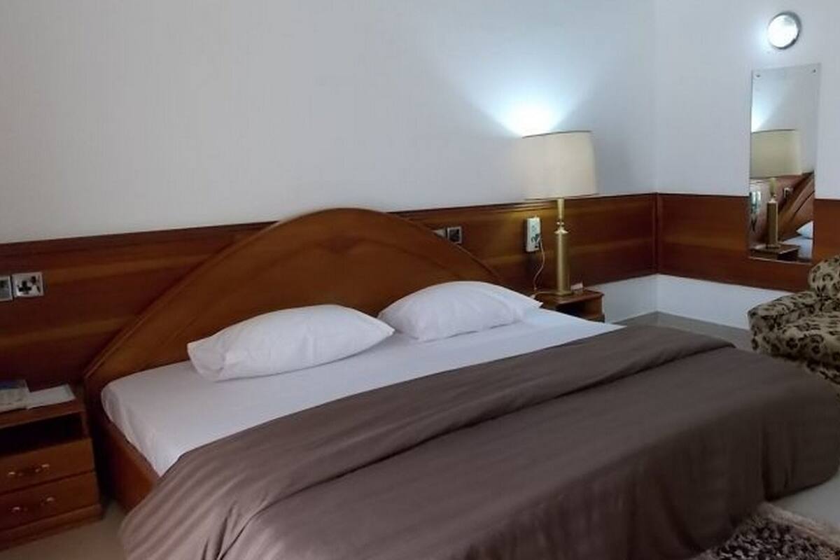A hotel room with a wooden headboard, a single bed with white and brown bedding, a bedside table with a lamp, and a mirror on the wall.