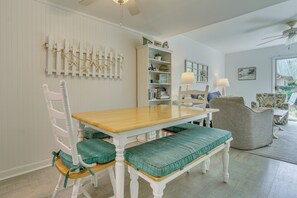 Un coin repas avec une table en bois et des chaises blanches, une bibliothèque et une vue sur l’extérieur.