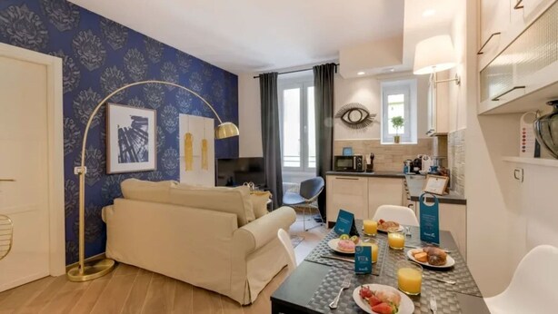 Una sala de estar moderna con un sofá, una mesa de comedor dispuesta para el desayuno y una cocina al fondo.