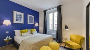 Un dormitorio con una cama, dos lámparas de noche, una silla y una ventana con cortinas.