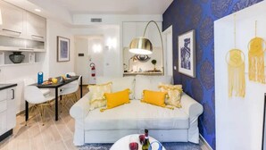 Un espacio habitable compacto con kitchenette, zona de comedor y sofá con cojines amarillos.