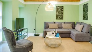 Ein Wohnzimmer mit grauem Sofa, einem runden Couchtisch, einem Fernseher auf einem Standfuß und einer Stehlampe.