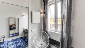 A modern hotel room with a large window, a white fan, a chair, and a mirror. - Sweett | Duomo View V (Milano)
