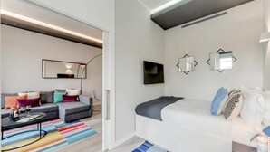 A modern hotel room with a grey sofa, a white bed, and a colorful striped rug. - Sweett | Duomo View V (Milano)