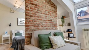 A modern living room with a brick accent wall, a sofa with green and white cushions, a side table with a lamp, and a view of the outside through a skylight. - Sweett | Sempione I - One Bedroom Apartment, Sleeps 2 (Milano)