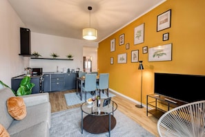 A modern living room with a sofa, coffee table, and TV stand. There is a kitchen area with a sink and cabinets.