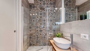 Een moderne badkamer met een douchecabine van glas, patroon betegelde vloeren, een houten wastafelmeubel en een grote spiegel.