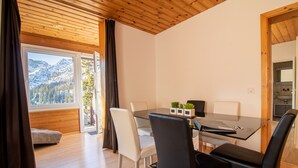 A modern dining area with a glass table, white and black chairs, and a view of mountains through large windows. - Miraflor Carmen (Arosa)
