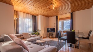 A modern living room with a large sectional sofa, a TV, and a dining area with a table and chairs. - Miraflor Carmen (Arosa)
