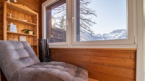 A cozy room with a cushioned seating area, wooden shelves, and a large window offering a mountain view. - Miraflor Carmen (Arosa)