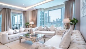A spacious living room with a large sofa set, a glass coffee table, and a view of the cityscape through large windows.