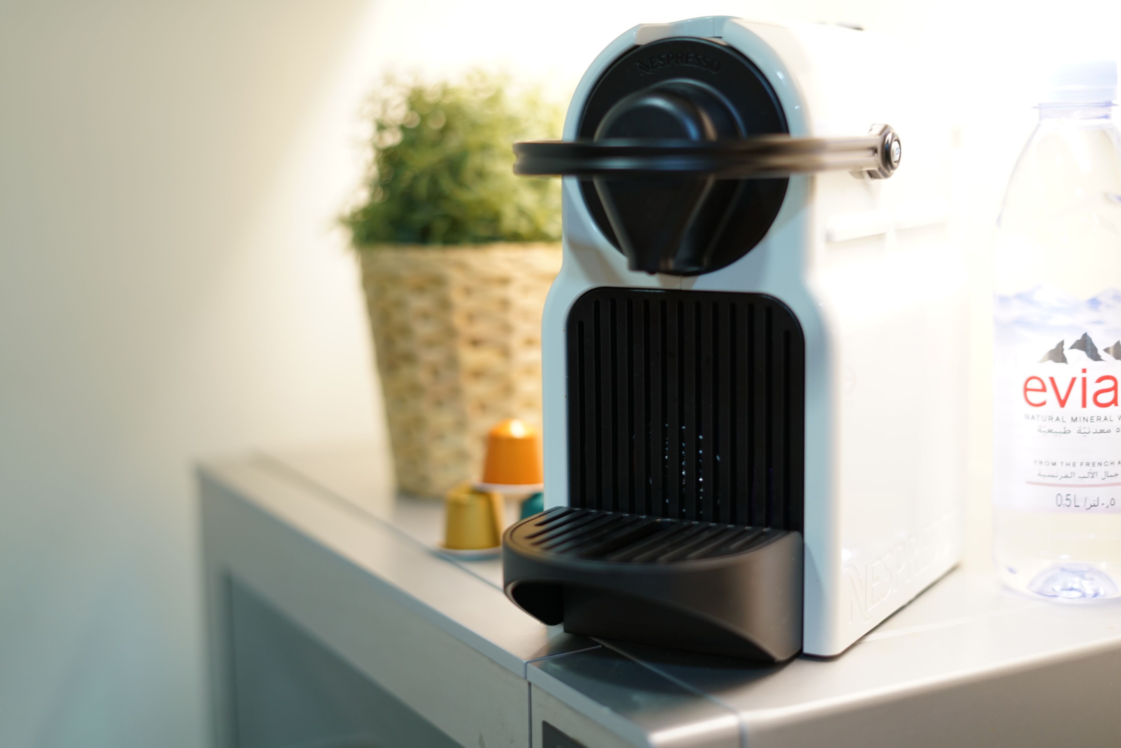 A coffee machine on a counter with a bottle of Evian water nearby.