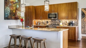 A modern kitchen with wooden cabinets, a large island with stools, a built-in microwave, and a hanging light fixture.