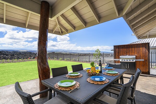 An outdoor dining area with a view of the landscape, a grill, and a table set with plates and cutlery.