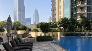 A rooftop pool area with lounge chairs, a swimming pool, and a view of tall buildings in the background.