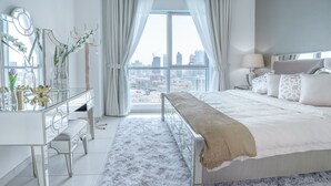 A modern bedroom with a large bed, a vanity with a mirror, and a view of the cityscape through large windows.