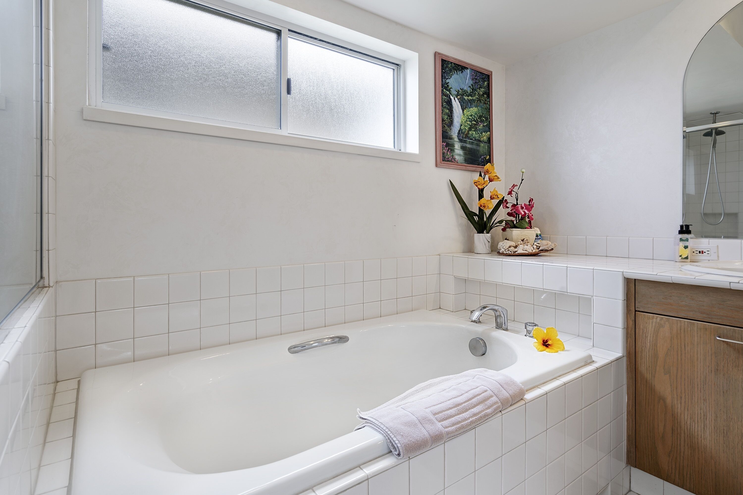A bathroom with a bathtub, a window, a sink, and a mirror.