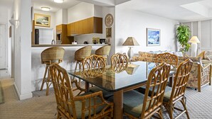 A modern kitchen with wooden cabinets, a glass dining table, and wicker chairs. - Vista Waikoloa B-206 2 Bedroom Condo by RedAwning (Waikoloa)