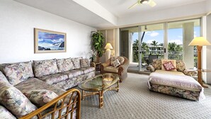 A living room with a sofa, armchairs, a glass coffee table, and a ceiling fan. - Vista Waikoloa B-206 2 Bedroom Condo by RedAwning (Waikoloa)
