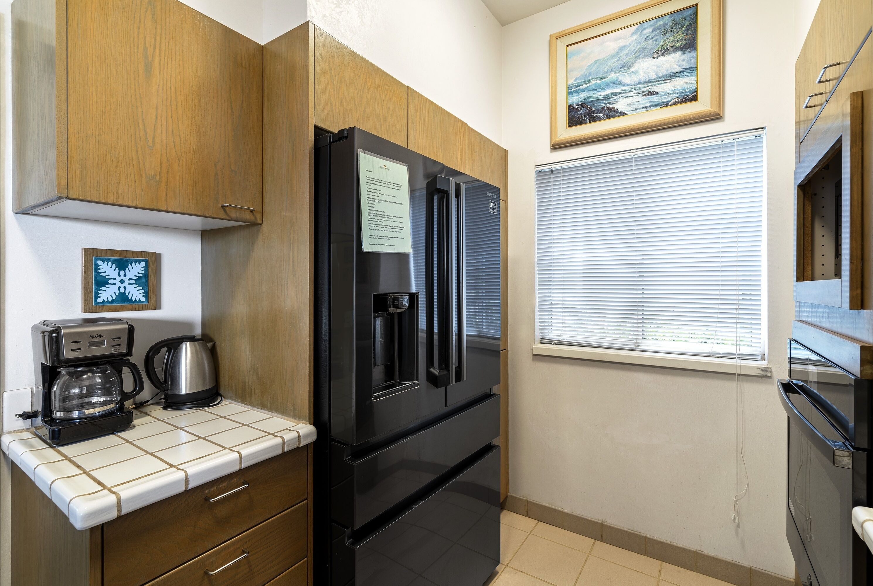 A modern kitchen with wooden cabinets, a black refrigerator, a coffee maker, and a window with blinds.