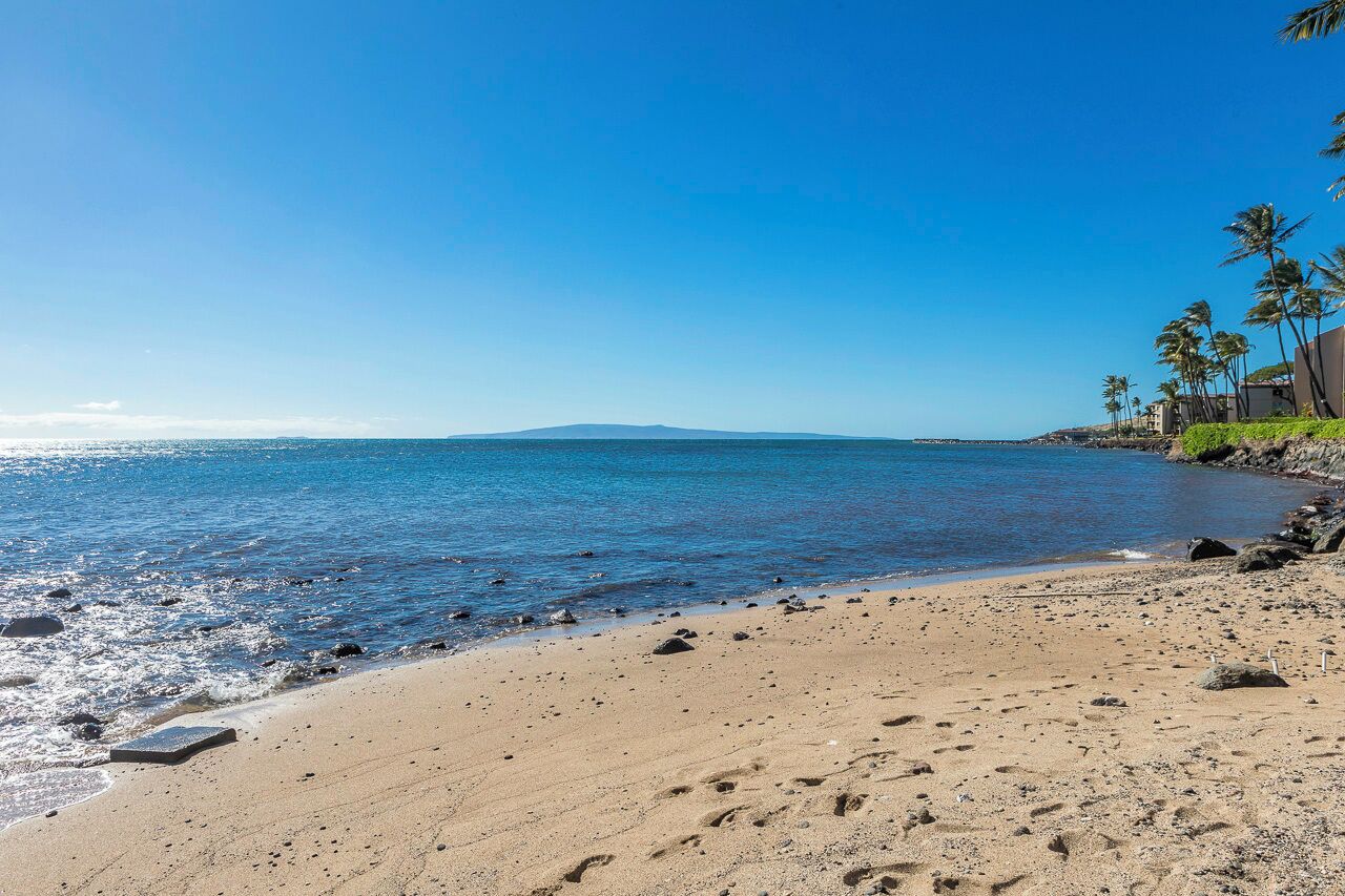 A beach with clear blue water, a sandy shore, and a distant mountain.