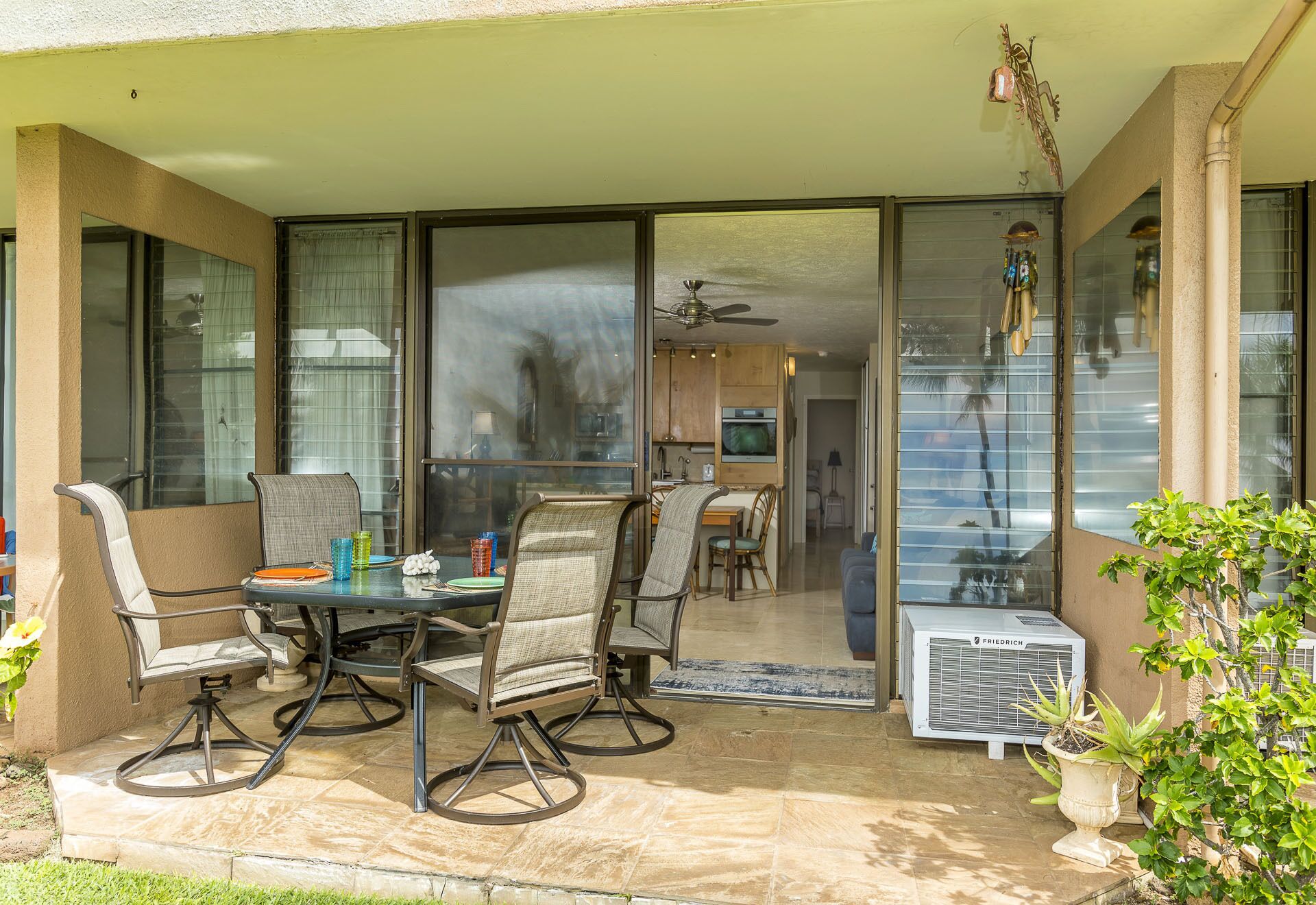 Eine Terrasse im Freien mit Esstisch und Stühlen, einem Deckenventilator und Blick ins Haus.