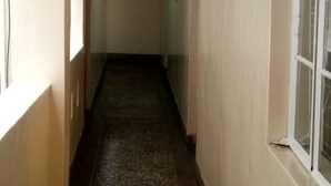 Um corredor estreito com chão ladrilhado, uma janela à direita e uma porta no final.