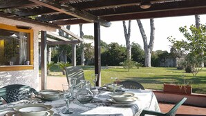 An outdoor dining area with a table set for four, surrounded by chairs, and a view of a grassy yard with trees. - Magnificent Depandance with Pool in Villa 900 mt from the beach (San Felice Circeo)