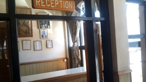 A reception area with a wooden bench, framed certificates on the wall, and a sign that reads "RECEPTION". - Hotel Joska (Nakuru)