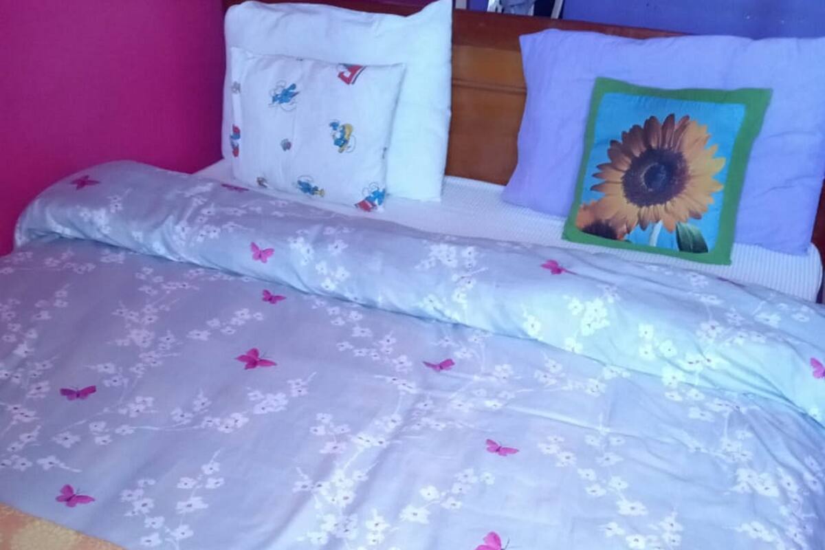 A bed with floral and butterfly-patterned bedding, a wooden headboard, and a pillow with a sunflower design.