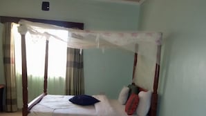 A bedroom with a four-poster bed, a green rug, and a suitcase.