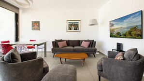 A modern living room with a grey sofa, a wooden coffee table, and a large painting of a coastal landscape.