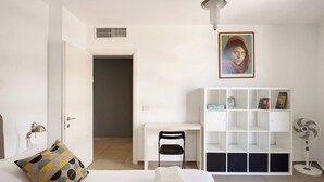 A bedroom with a bed, a desk, a chair, a bookshelf, and a fan.