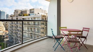 A balcony with a view of a cityscape, a table with colorful chairs, and a modern building with balconies.