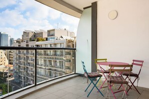 Varanda com vista para um horizonte urbano, uma mesa com cadeiras coloridas e um edifício moderno com varandas.