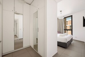 Quarto de hotel com cama, guarda-roupa, espelho e janela com cortinas.
