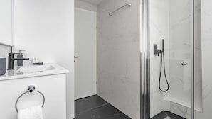 Une salle de bain moderne avec une douche à parois de verre, un lavabo blanc avec un miroir au-dessus et un porte-serviettes mural.